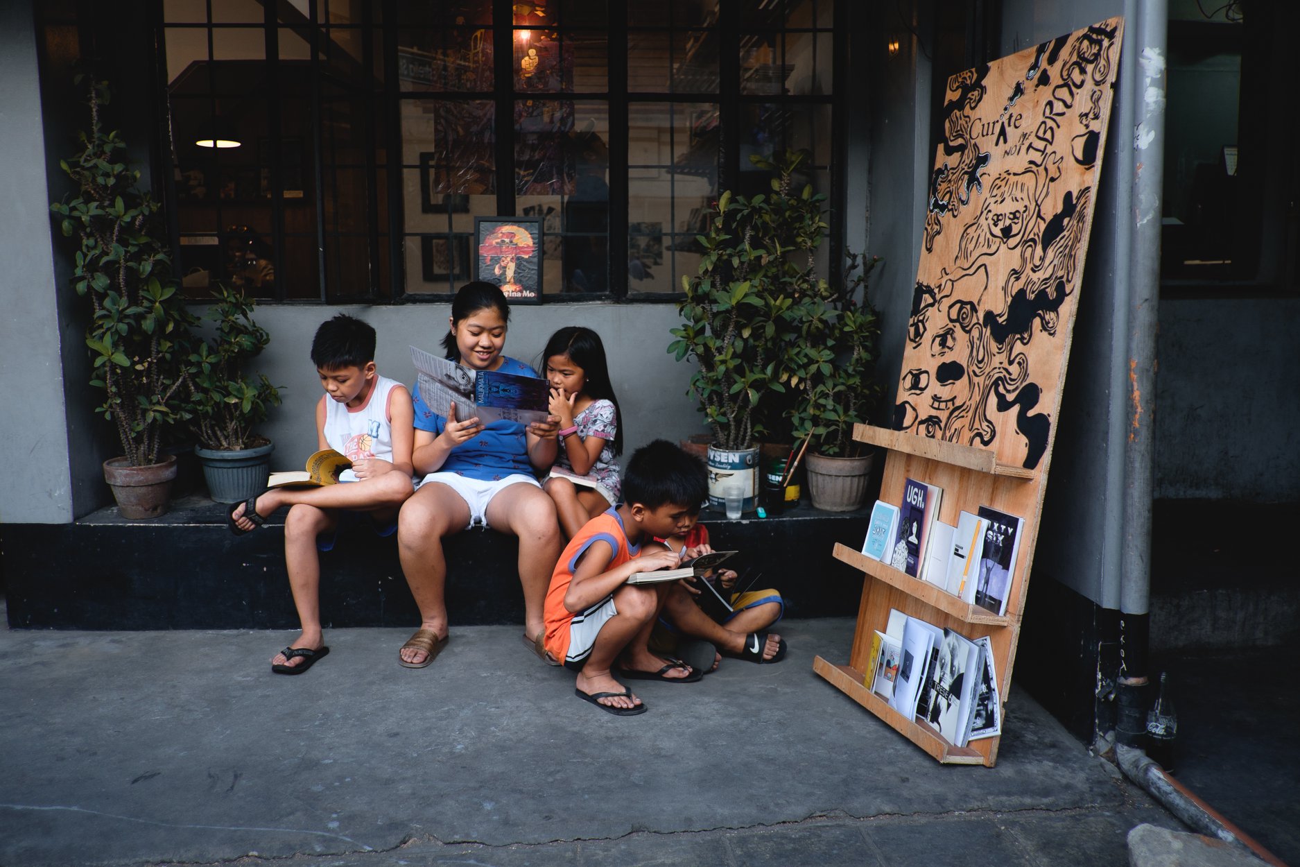 A group of children sitting outside of a café reading books.